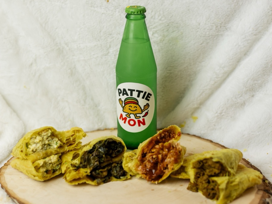 A green Pattie Mon bottle on a wooden board with four patties cut open in front of it